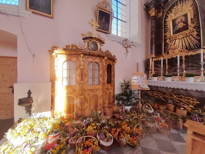 Barocker Beichtstuhl neben dem Seitenaltar, davor Blumen und Kräuter
